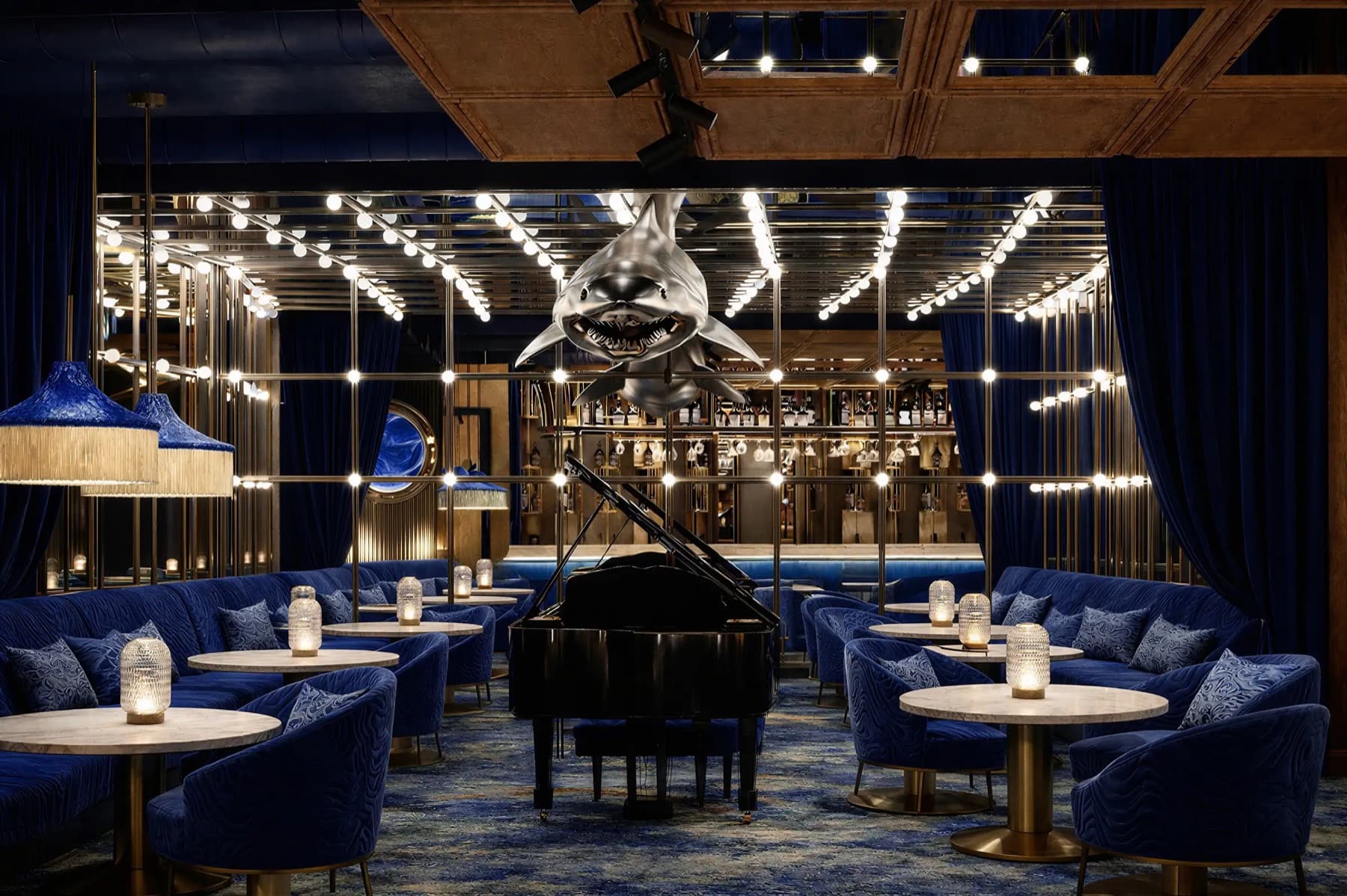 Haifisch's navy velvet lounge with a grand piano beneath a hanging shark sculpture, a cocktail bar in Zürich curated by Meetz