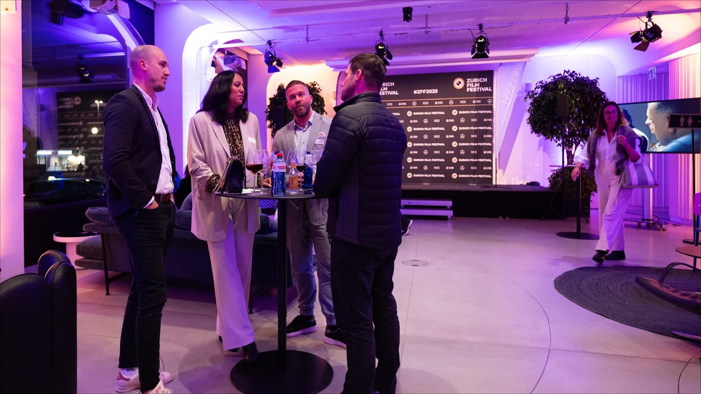 Guests at an apéro in front of a branded step-and-repeat wall