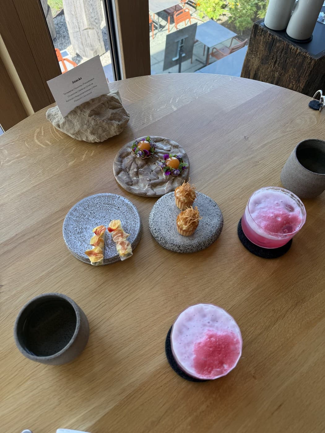 Four snack courses on stone plates, the menu card on a river stone